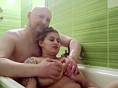 An older man relaxes in the bath while she gives him a handjob with her big natural tits