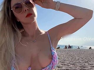 Seksikäs blondi riisuu julkisella rannalla, näyttää kauniit tissit ja kimmoisan perseen